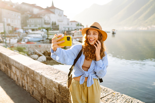 Beautiful tourist walks the streets and takes selfie using smartphone camera. Lifestyle, travel, rest, weekend, active life.