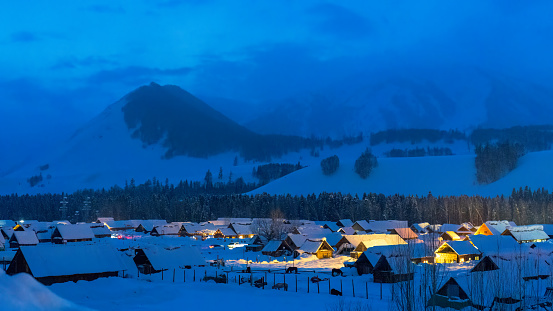 The northern village surrounded by woods and snow under the snow-capped mountains is very peaceful at night