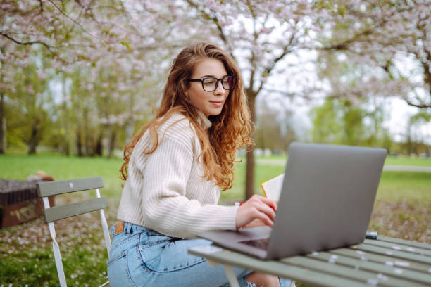 istock Beautiful woman sitting on blooming park and using laptop. 2148188213