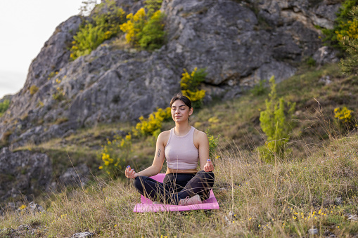 Front view of the young girl meditating on a meadow  surrounded by hills during the spring day