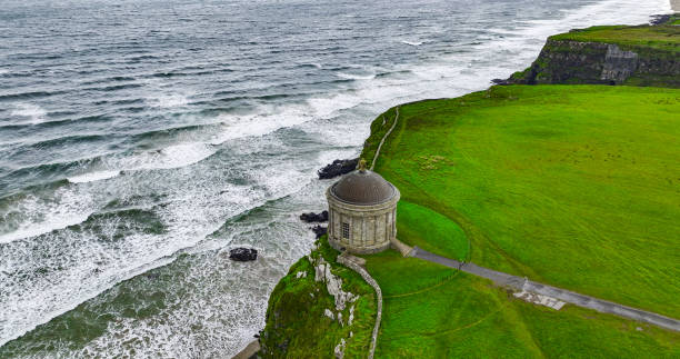 Aerial view of Mussenden Temple library in Northern Ireland, Downhill, County Londonderry, Ruin of Mussenden temple on the edge of a cliff, Aerial view of Causeway Beach and Mussenden Temple, Mussenden Temple on high cliffs near Castlerock
Mussenden Temple is located in the beautiful surroundings of Downhill Demesne near Castlerock in County Londonderry. It perches dramatically on a 120 ft cliff top, high above the Atlantic Ocean on the north-western coast of Northern Ireland, offering spectacular views westwards over Downhill Strand towards Magilligan Point and County Donegal and to the east Castlerock beach towards Portstewart, Portrush and Fair Head. aerial view of mussenden temple library in northern ireland, downhill, county londonderry, ruin of mussenden temple on the edge of a cliff, aerial view of causeway beach and mussenden temple, mussenden temple on high cliffs near castlerock