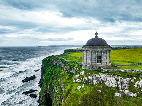 Aerial view of Mussenden Temple library in Northern Ireland, Downhill, County Londonderry, Ruin of Mussenden temple on the edge of a cliff, Aerial view of Causeway Beach and Mussenden Temple, Mussenden Temple on high cliffs near Castlerock

Mussenden Temple is located in the beautiful surroundings of Downhill Demesne near Castlerock in County Londonderry. It perches dramatically on a 120 ft cliff top, high above the Atlantic Ocean on the north-western coast of Northern Ireland, offering spectacular views westwards over Downhill Strand towards Magilligan Point and County Donegal and to the east Castlerock beach towards Portstewart, Portrush and Fair Head.