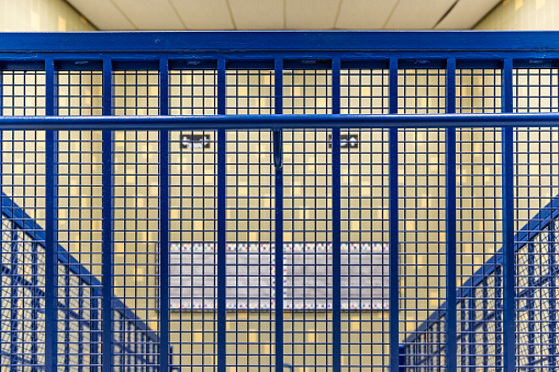 Close-up photo of a blue metal railing at the top of a school staircase and tile wall.