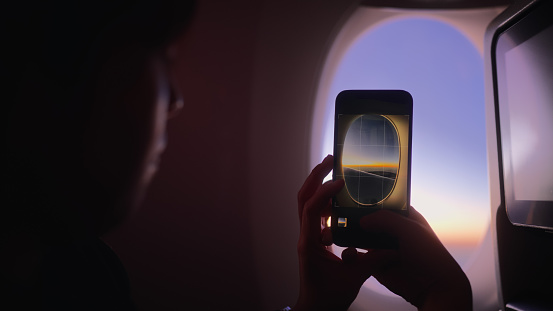 A female tourist is taking photos from the window of an airplane with her mobile smart phone.