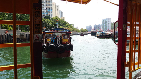 Hong Kong - 07.11.2021: A kaito, a traditional motorised ferry, filled with passengers approaching Pontoon outside Marina Habitat in Aberdeen West Typhoon Shelter on a sunny day during the pandemic