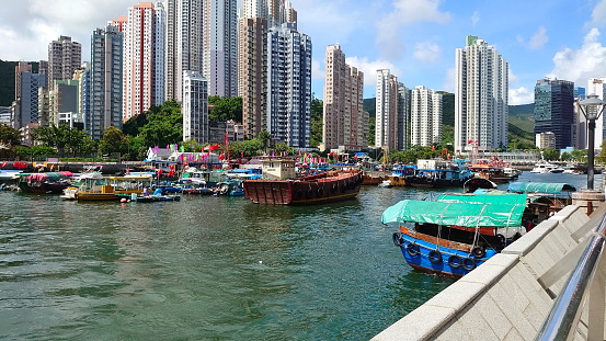 Hong Kong - 07.11.2021: Boats and yachts berthed in Aberdeen West Typhoon Shelter on a sunny day with skyscrapers in the back during the pandemic, viewed from the Ap Lei Chau side