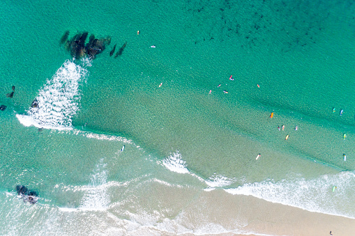 Scenic aerial of people riding on surfing boards on a beach. Top down view of surfers trying to catch waves in a turquoise water. Summer concept