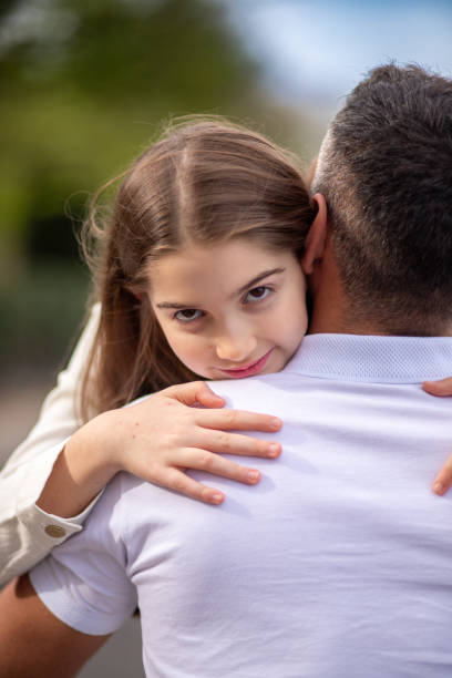 istock Young girl tightly embraces her father, looking into the camera. 2148192425