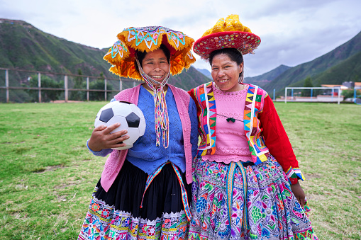 Two women of the Quechua ethnic group with the soccer ball looking at the camera and smiling on the soccer field