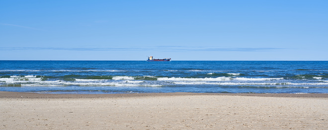 Distant view of cargo container ship on seascape with beautiful horizon and clear blue sky seen through beach at Hirtshals, Jutland, Denmark