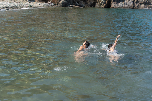 Two swimmers enjoy the clear sea, with rocky shores in the distance.
