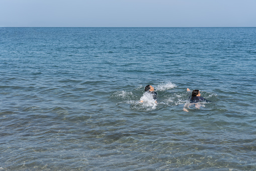 Two swimmers enjoy the sea, splashing in the water.