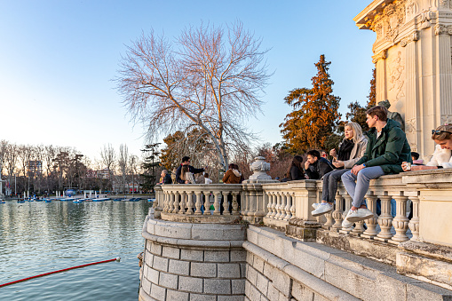 March 4th, 2023. Various persons enjoying the sunny spring afternoon by a pond in the central park of Madrid,