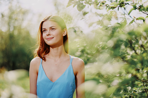 Woman smile with teeth in profile happiness in nature in the summer near a green tree in the garden of the park in a blue dress, the concept of women's health and beauty with nature sunset. High quality photo