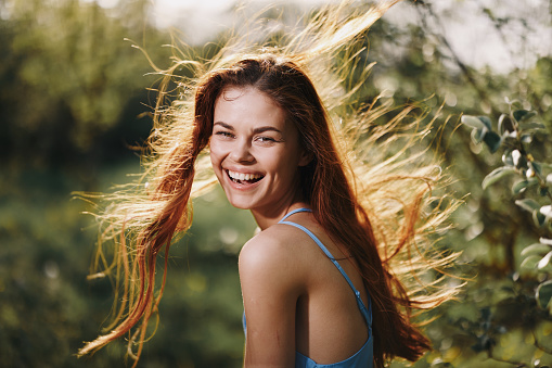 Woman portrait smile happiness catch looks into the camera with a smile with teeth spring flying hair long red, the concept of health and beauty hair sunset. High quality photo
