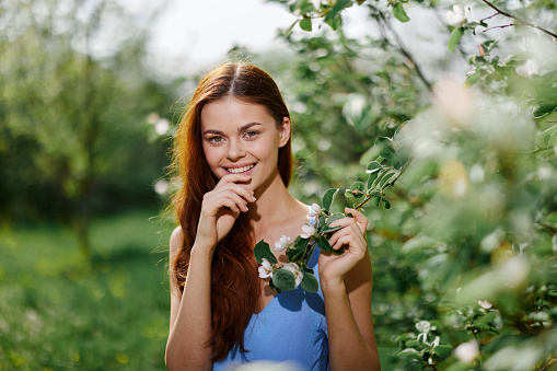 Woman portrait beautifully smiling with teeth spring happiness in nature against a green tree tenderness hand touching a branch of a blooming tree, safety from allergies and insects. High quality photo