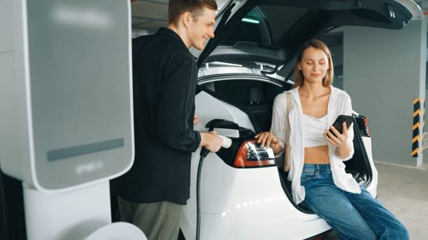istock Electric car driver checks battery charging status app screen in car innards 2148200018