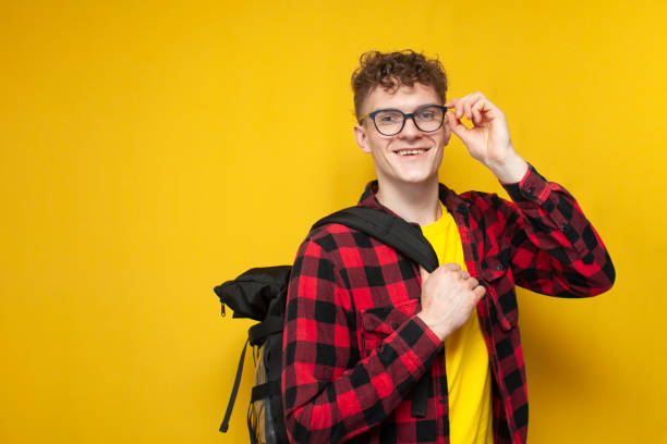 istock young curly guy student in glasses with a backpack stands on a yellow background smiling and looking at the camera 2148200889