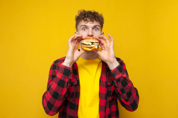istock curly guy student eats a burger on a yellow background, a man with fast food 2148200900