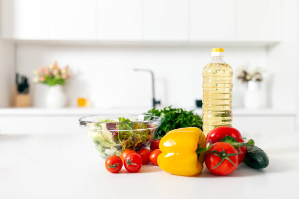 ingredients for salad and products lie on the table in white modern kitchen, greens, tomatoes, peppers, bottle of oil in empty light kitchen, healthy vegetarian food