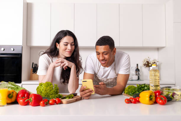 young multiracial couple looking at phone and checking grocery list in white modern kitchen