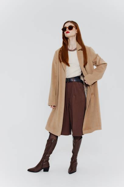 istock An elegant red-haired lady with glasses and a beige coat poses full-length on a white background in the studio for a showroom advertisement. Cool offer for brands 2148202010
