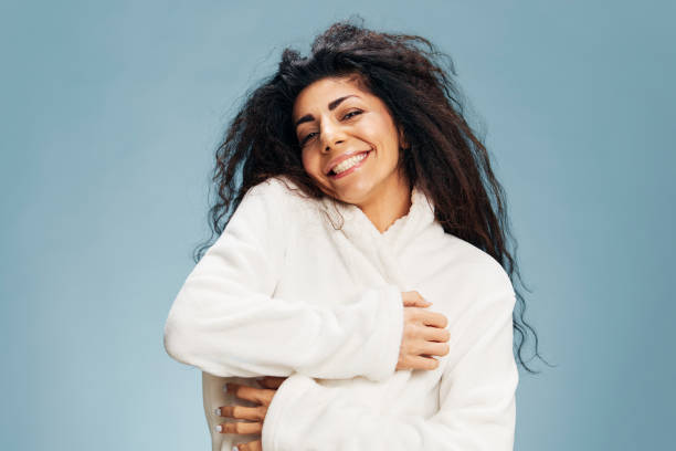istock SPA PROCEDURE CONCEPT. Cheerful pretty tanned happy curly Latin lady touching bathrobe both hands, hugs herself smiling posing isolated on pastel blue background, look at camera. Copy space offer 2148204610