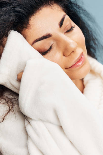 istock SPA PROCEDURE CONCEPT. Smiling happy curly Latin lady enjoy soft bathrobe touching face, recline on hands, sleeping, posing isolated on pastel blue background, closing eyes. Copy space, beauty banner 2148205222