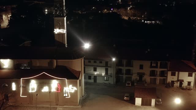 Orbit 4k drone night flying above medieval Italian catholic church decorated with illuminated Christmas figures