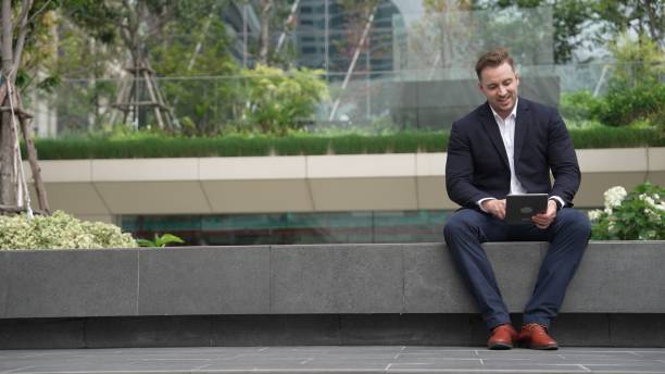 istock Businessman sitting at park while working on tablet by reading report. Urbane 2148209568