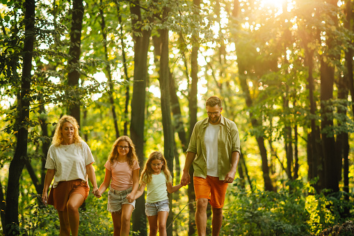 An adventurous family is holding hands in forest and exploring nature while hiking. Portrait of a happy family spending sunny summer day in nature together. A young family exploring wilderness.
