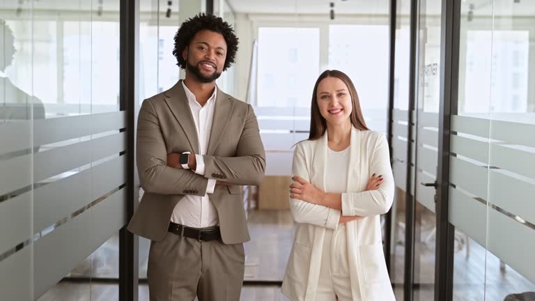 A young businessman and his female colleague stand with arms crossed