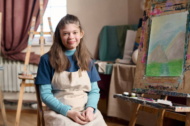istock Girl with Williams Syndrome Sitting by Easel in Art Studio 2148215078