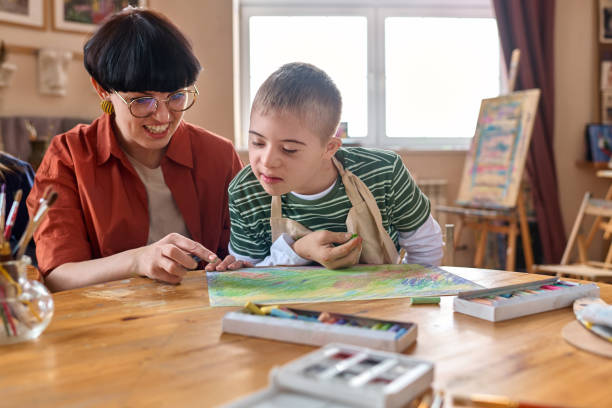 istock Boy with Down Syndrome Enjoying Art Class with Woman Assisting 2148215082