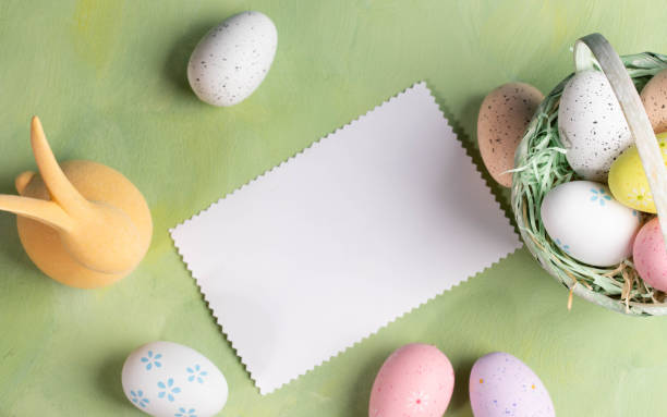 istock White blank note, decorative Easter eggs, yellow bunny on pastel yellow green backdrop. Top view. 2148215348