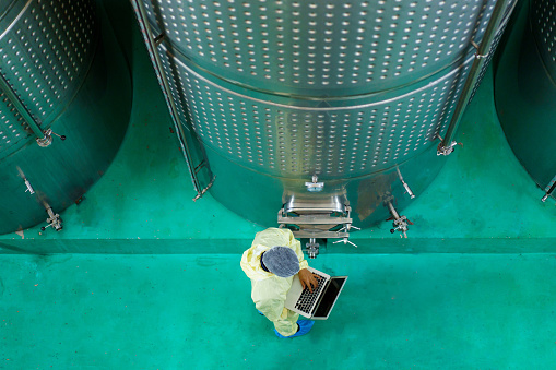 Head of quality control officer examines inside the food and beverage manufacturing factory. Female food scientist is checking a fermentation tank in the beverage factory.