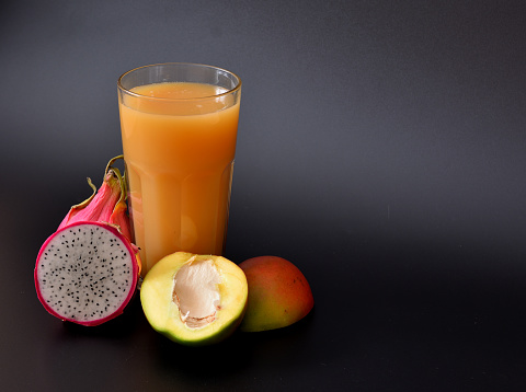 Drink juice in a tall faceted glass on a black background, next to ripe fruits. Close-up.