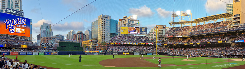 San Diego, California, United States - 4/18/2023: A wide panorama of Petco Park during a game, as seen from the field level.  The stadium is full of spectators.  The skyline of San Diego downtown can be seen in the background.  Taken at dusk.