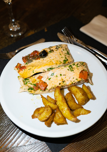 A plate of delicious pan-seared salmon with a side of potato wedges served in a restaurant in Italy.