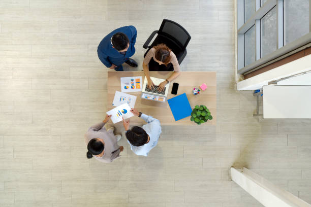istock Four business people meeting around a small table with document papers, folder, mobile phone and laptop computer. High angle view. 2148220266