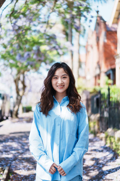 istock Young Asian woman standing under a tree looking directly into the camera 2148221012
