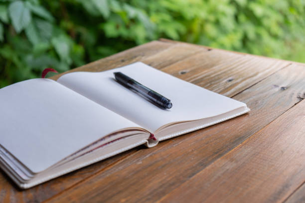 Open white empty paper notepad on wooden table outdoors. Concept of author writing in relaxed cozy atmosphere. Spiritual health digital detox slowing down