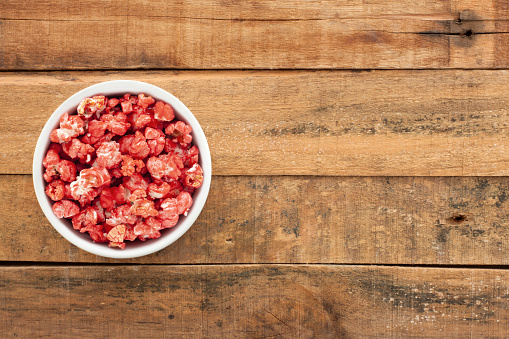Top view of white bowl full of red dyed popcorn over wooden table