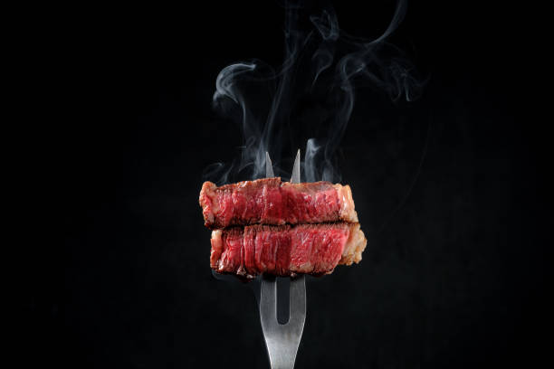 istock Sliced and steaming rare rib eye steak on a fork on a dark background 2148223637