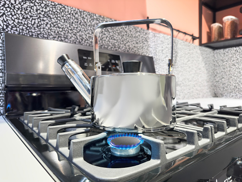 Stainless steel kettle heating up on a gas stove burner in a domestic kitchen
