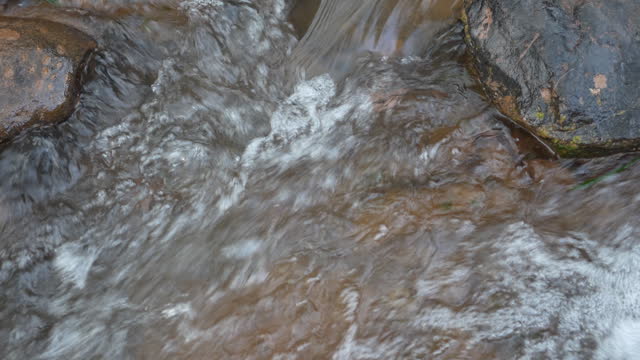 Clear stream running through stone boulders Abundant river flowing on stone bottom in slow motion. Wild mountain river water splashing in a summer day.