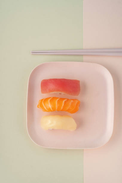 Three different sushi nigiri on a plate on a pink background with chopsticks