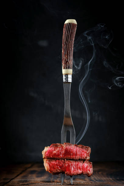 A vivid side-angle shot of grilled steaks and beef kebabs sizzling over a charcoal grill, surrounded by flames and glowing embers. The scene captures the smoky aroma, rich texture, and golden sear of perfectly cooked meat brushed with olive oil, herbs, and spices. Sparks rise from the fire as the heat enhances the color and juiciness of the roast, creating a powerful sense of flavor and appetite. Perfectly representing the energy of summer cookouts, outdoor grilling, and culinary passion, this image evokes warmth, craftsmanship, and the irresistible appeal of freshly barbecued food.