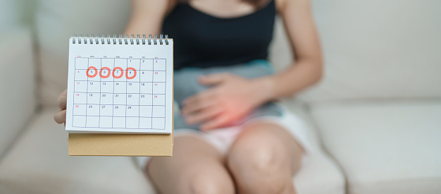 Menstruation period cycle of monthly and Stomachache concepts. woman having abdomen pain with hot water bottle and calendar, illness female suffer from premenstrual ache and body Health problem
