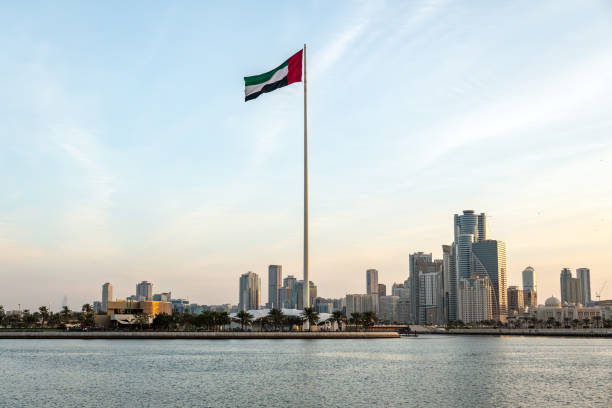 Flag of the United Arab Emirates in Sharjah on coastline in the background of tall skyscrapers. urban landscape Flag of the United Arab Emirates in Sharjah on the coastline in the background of tall skyscrapers. urban landscape sharjah city stock pictures, royalty-free photos & images